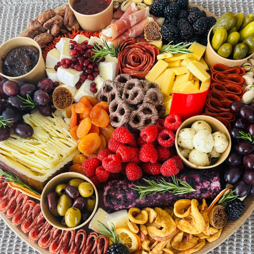 Charcuterie board close-up with cheese wedges, salami, prosciutto, raspberries, grapes, olives, pickles, and spreads