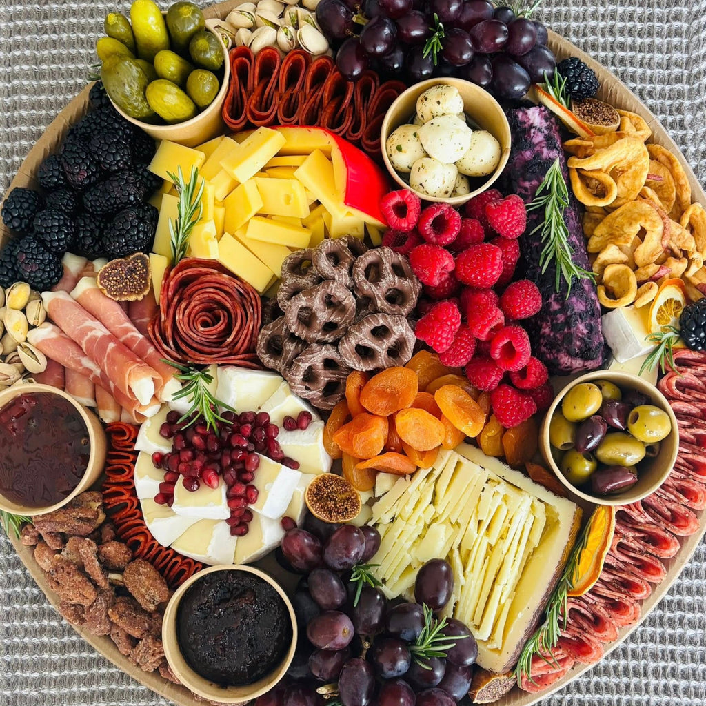 Charcuterie board with cheeses, cured meats, berries, grapes, pickles, olives, nuts, and sweet dips