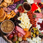 Charcuterie board close-up with salami rosettes, assorted cheeses, grapes, cherries, olives, mustard, and jam