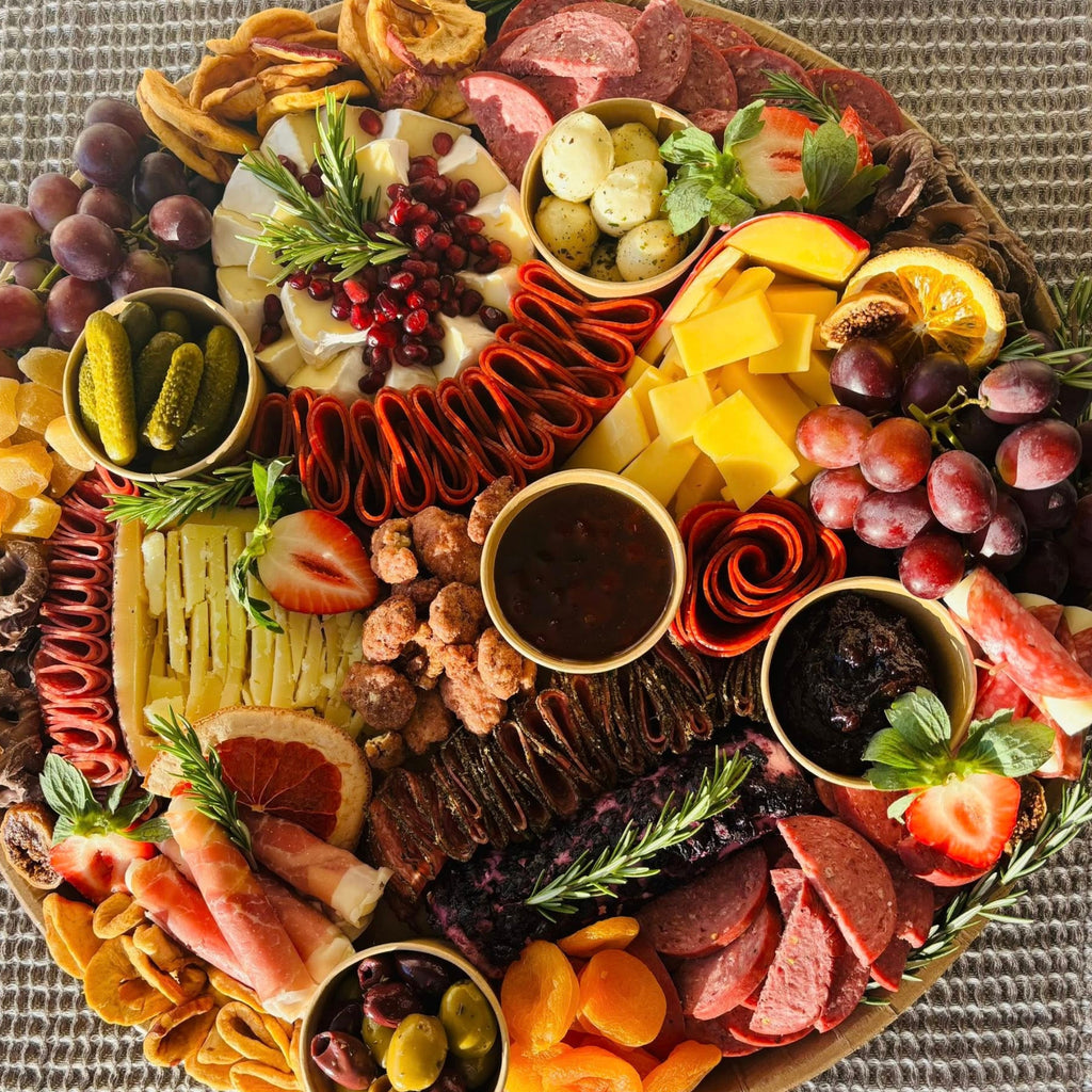 Charcuterie board with cured meats, mixed cheeses, grapes, pickles, olives, fig jam, and mustard dips