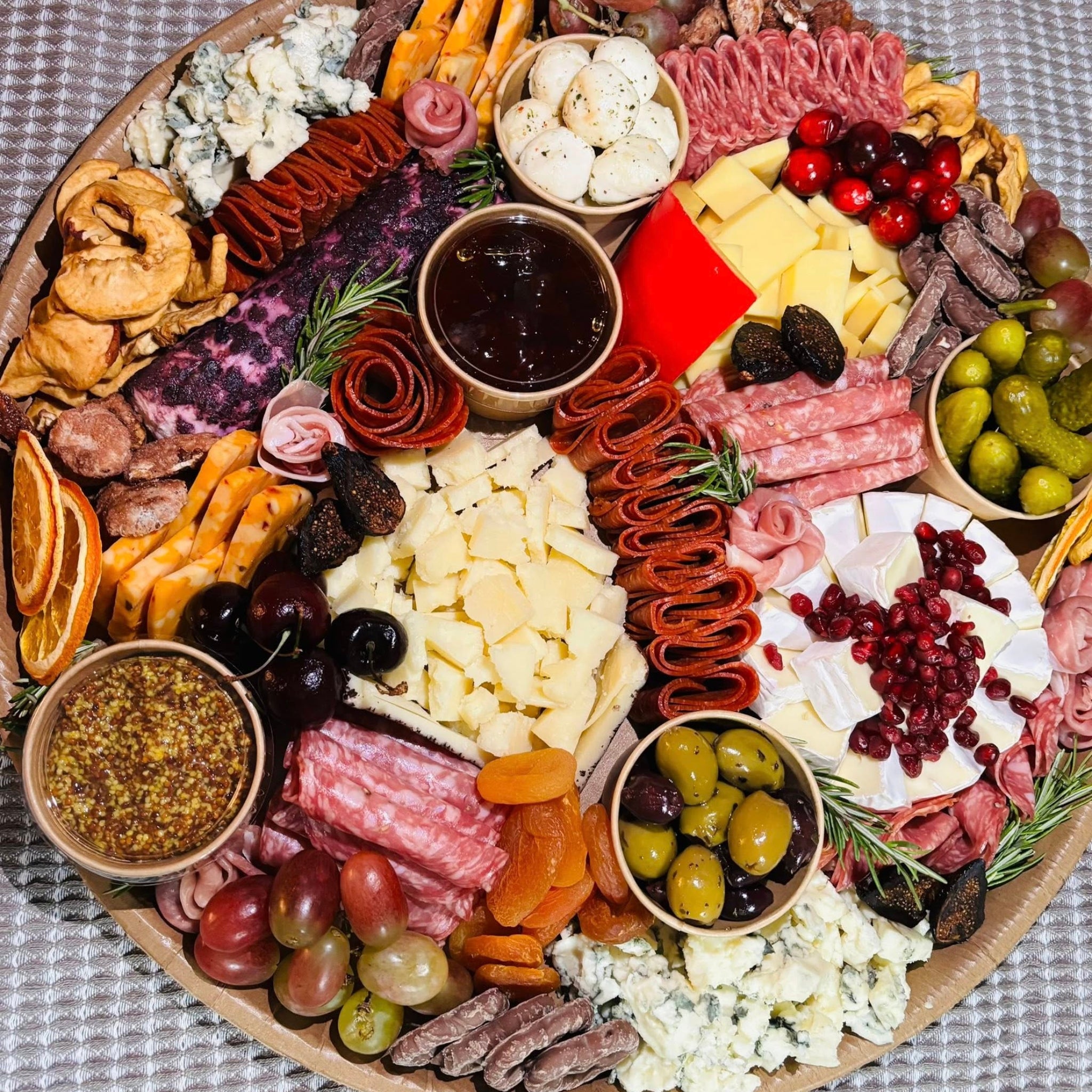 Charcuterie platter with cheeses, salami, pepperoni, grapes, olives, dried apricots, and jam and mustard dips