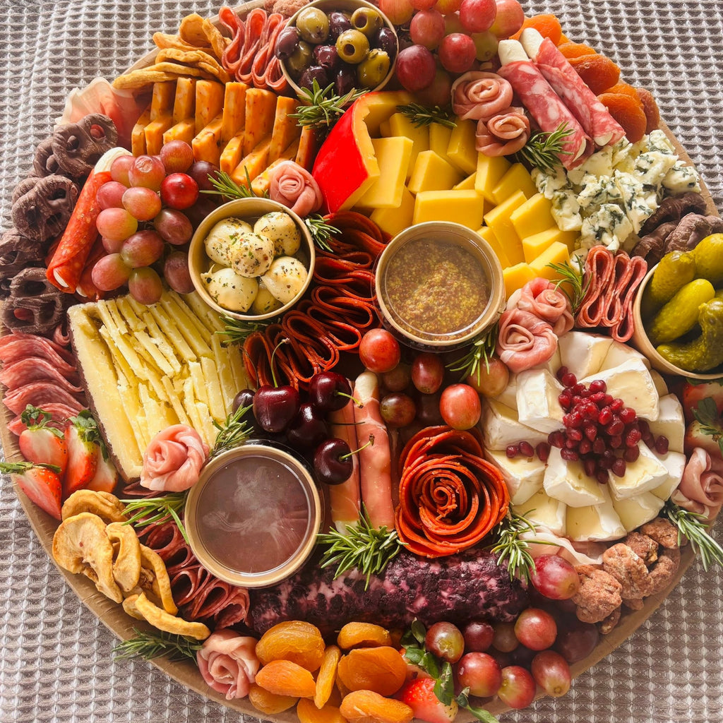 Charcuterie board with assorted cheeses, cured meats, grapes, cherries, olives, pickles, and dipping sauces