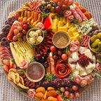 Charcuterie board with assorted cheeses, cured meats, grapes, cherries, olives, pickles, and dipping sauces