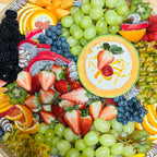 Fruit platter with grapes, strawberries, blueberries, blackberries, kiwi, citrus slices, and cream dip in a cantaloupe bowl