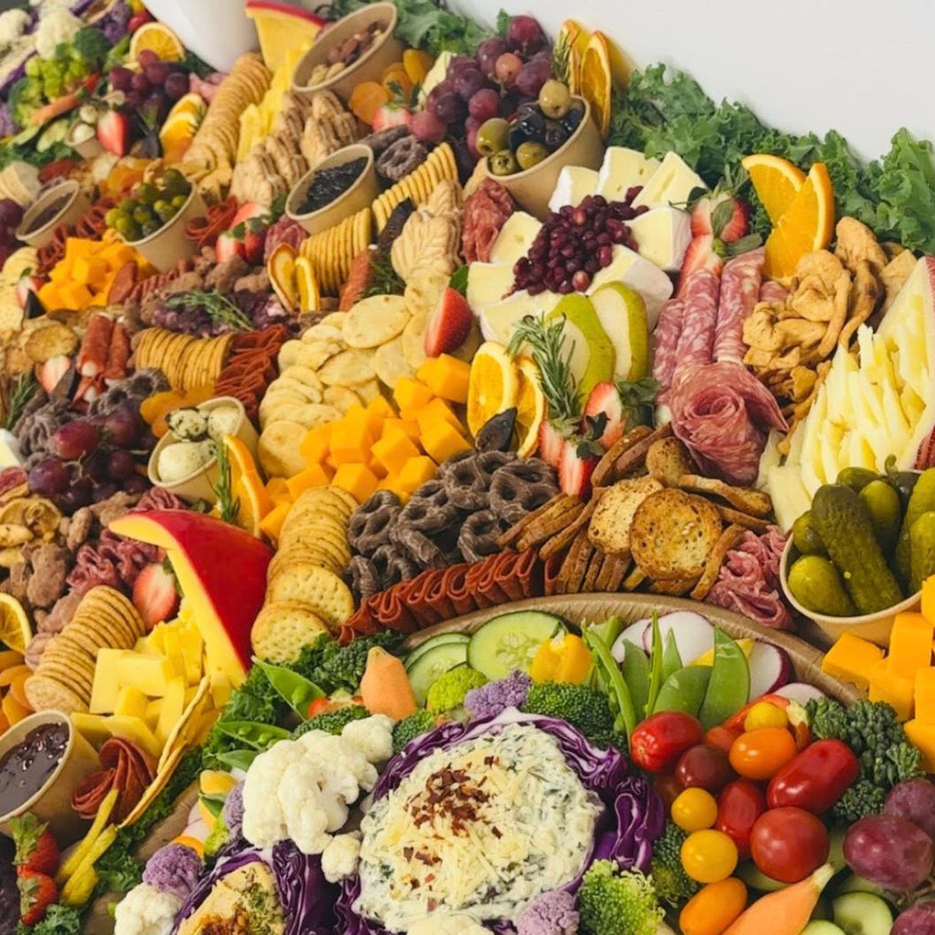 Grazing table close-up with cheese slices, salami, crackers, pickles, fruit, and a veggie tray with dip