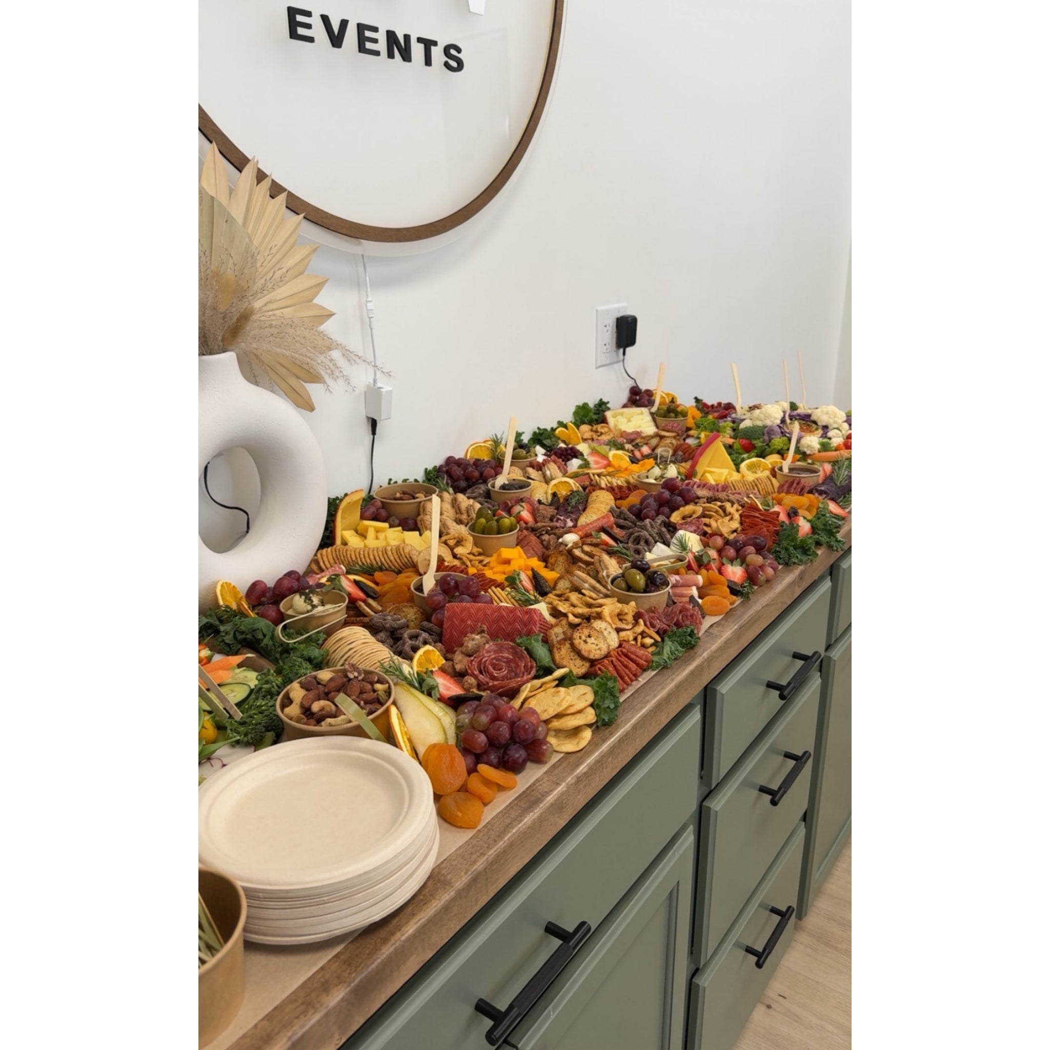 Event grazing table setup with charcuterie, cheese, fruit, crackers, and serving plates